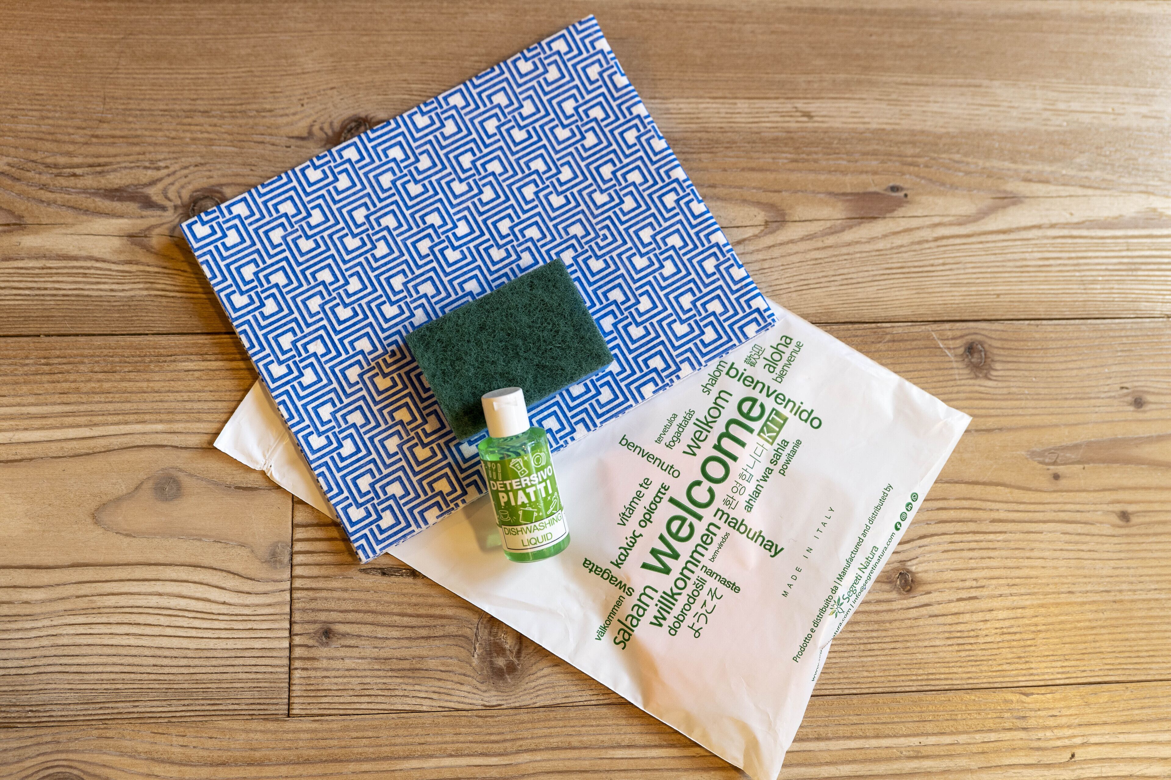 Un paño azul estampado, una esponja verde y una botella de lavavajillas sobre una superficie de madera.