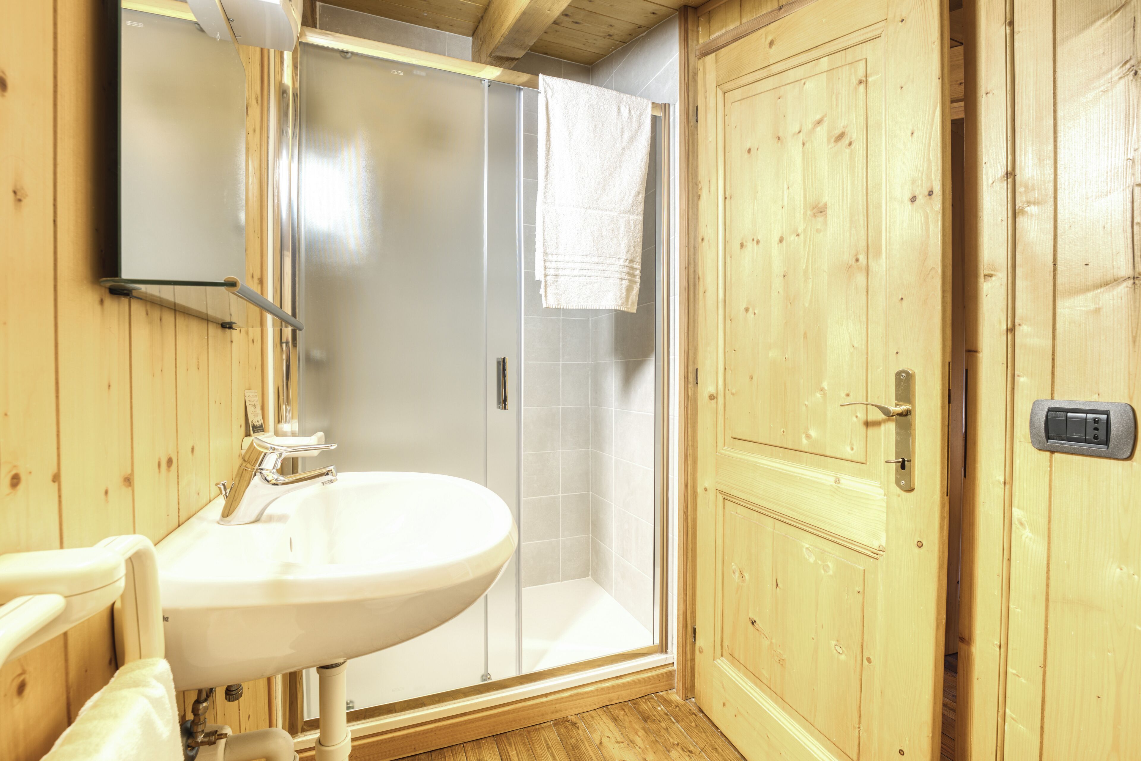 Un bagno in legno con lavabo, cabina doccia in vetro e porta in legno.