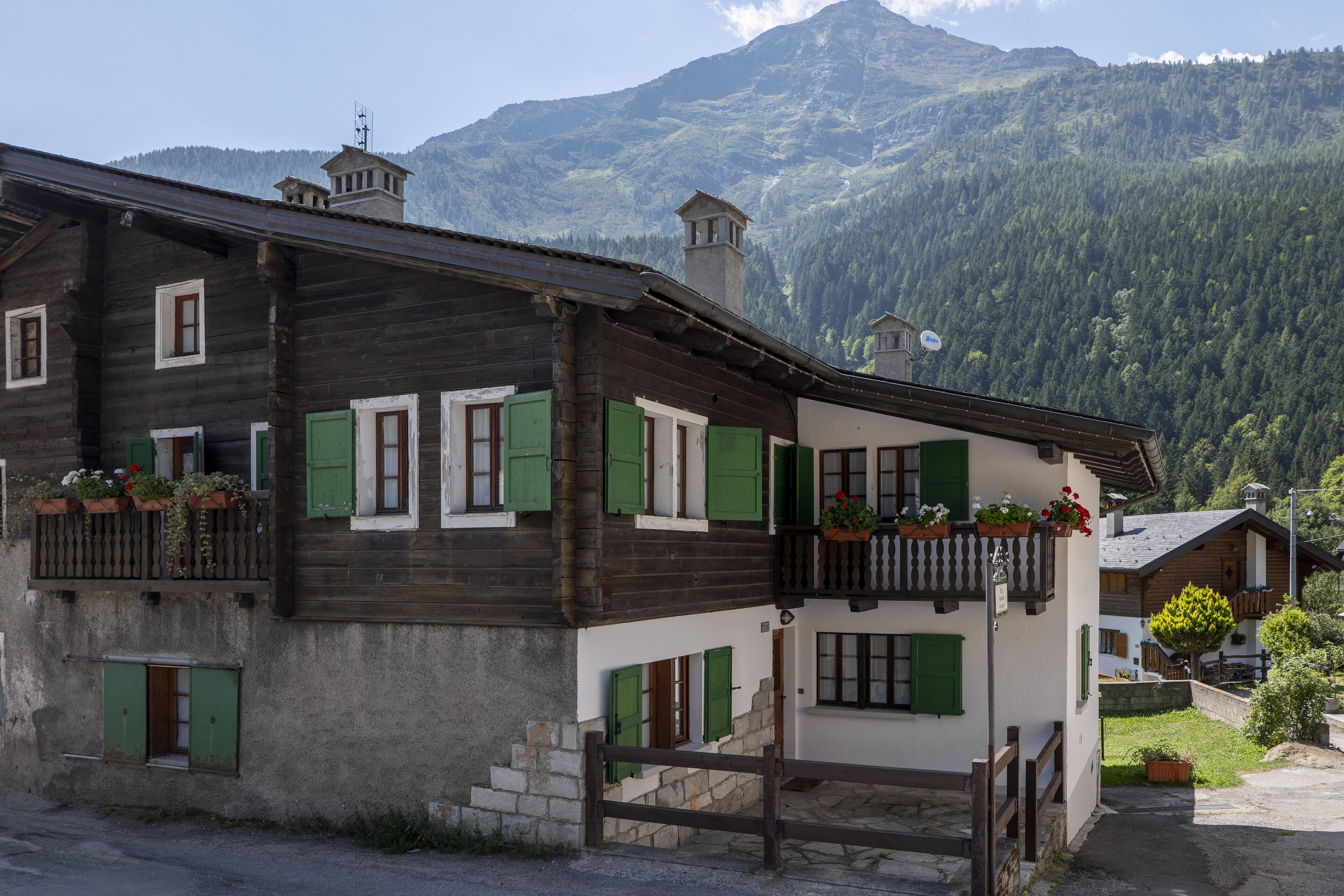 A traditional wooden house with green shutters and a stone staircase leading to a balcony.
