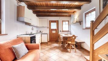 A cozy kitchen with wooden beams, a dining area with a table and chairs, and a sofa with a cushion.