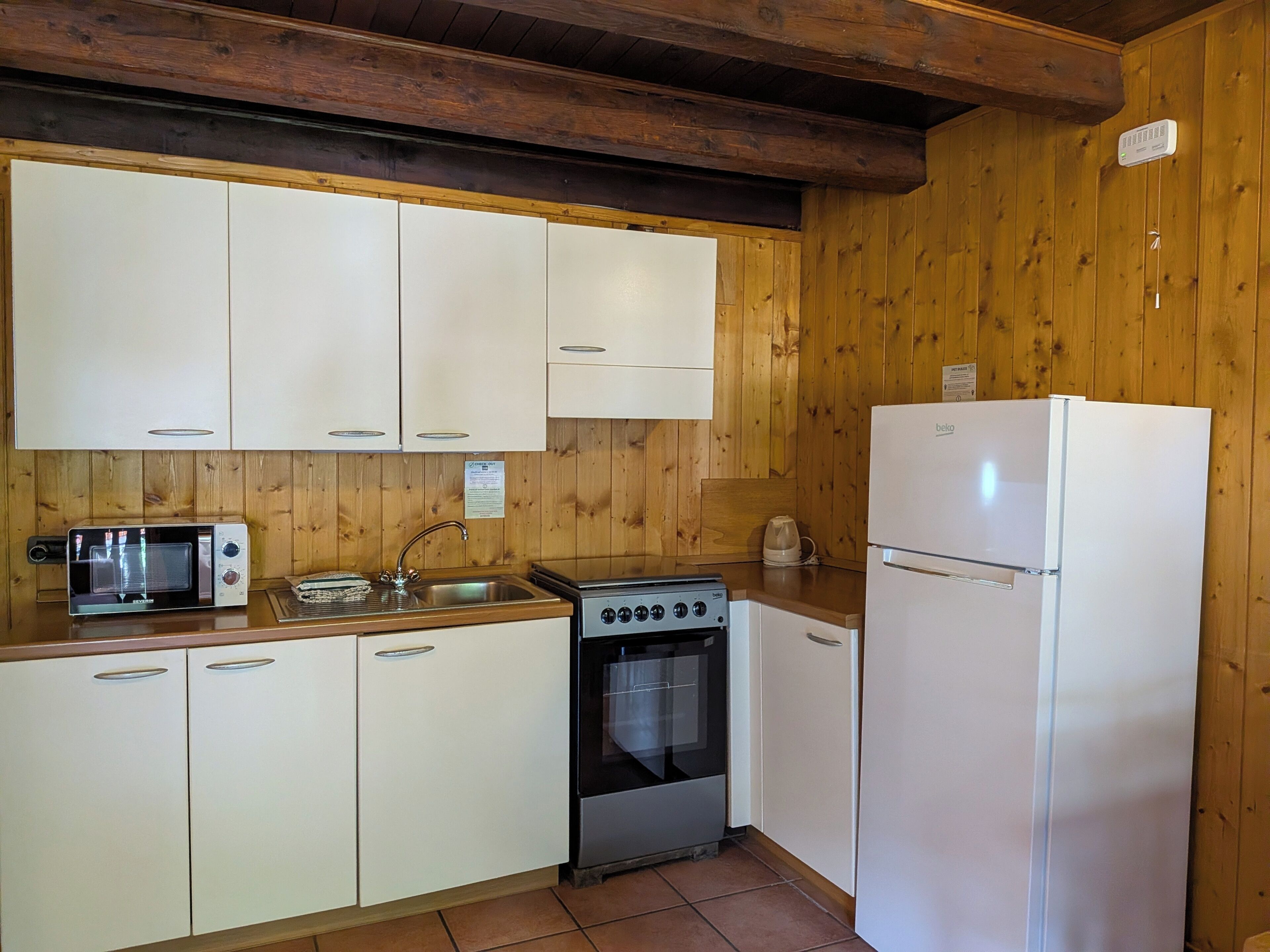 A kitchen with wooden walls, a stove, a microwave, a sink, and a refrigerator.