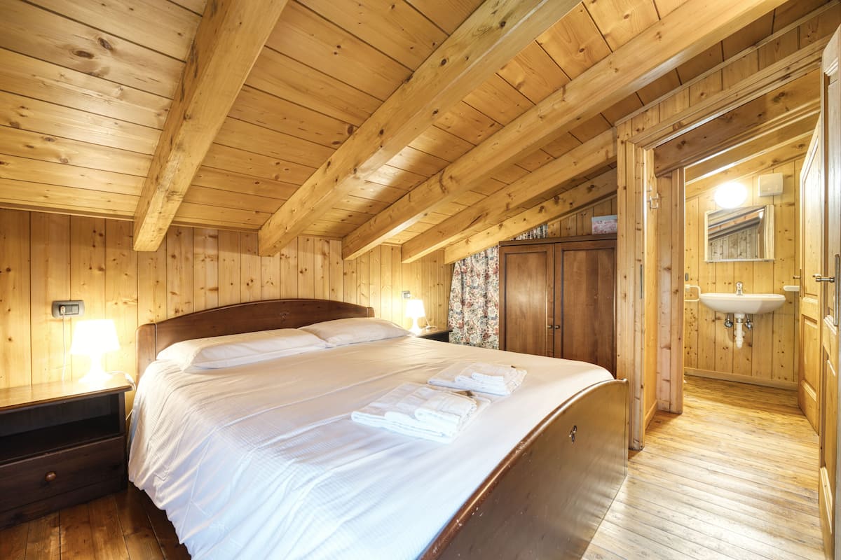 A wooden cabin room with a bed, a nightstand, a bathroom with a sink and mirror.