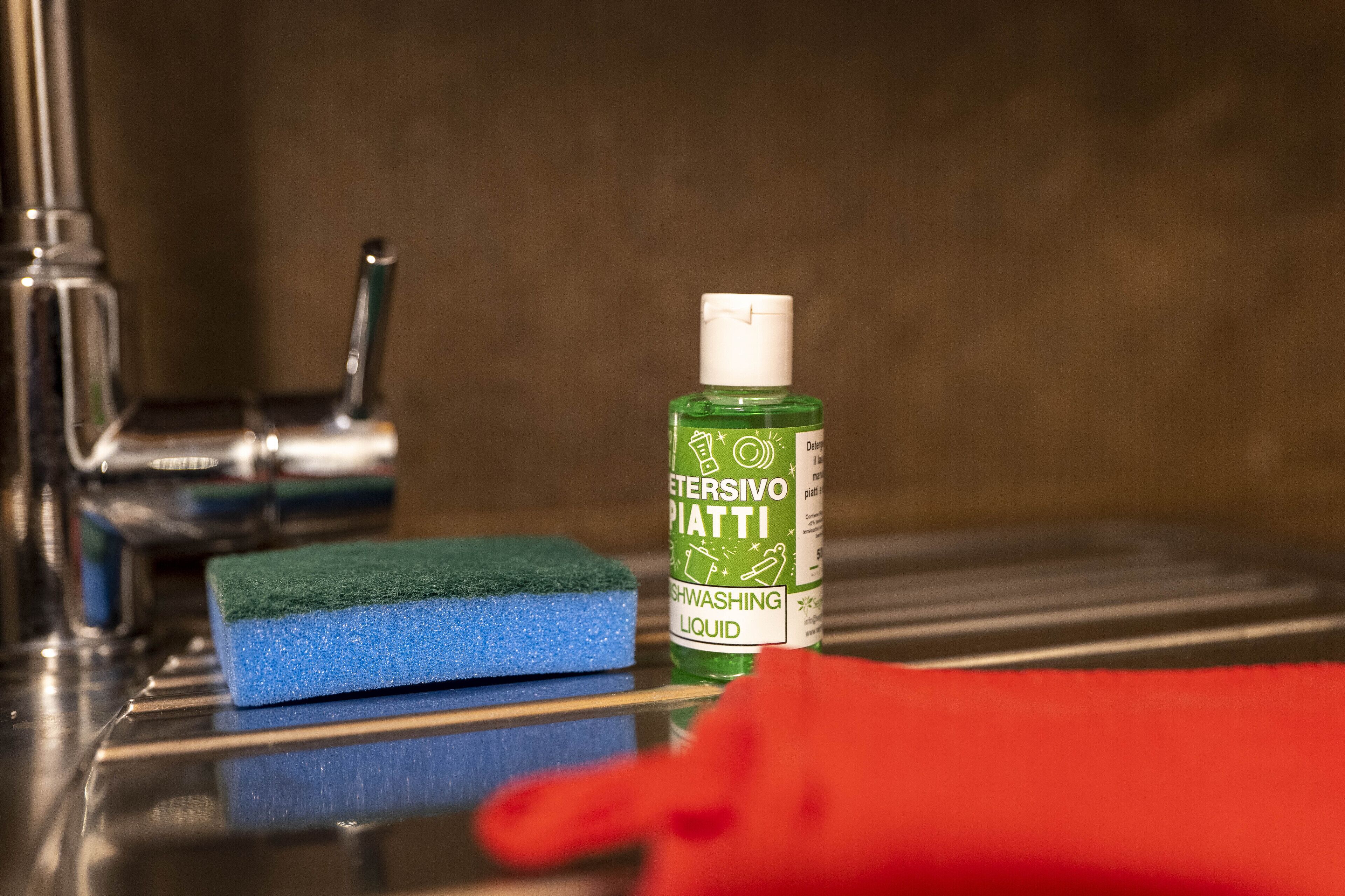 Un lavabo con una botella verde de detergente, una esponja azul y un paño rojo.