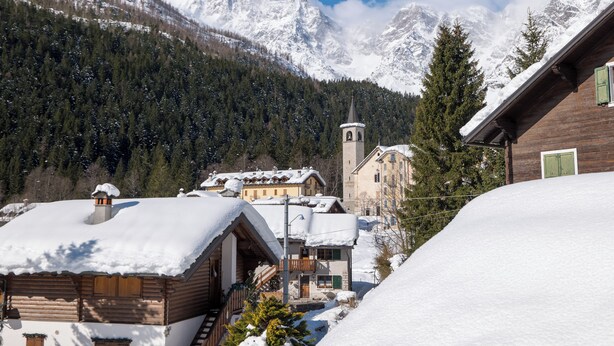 Een besneeuwd bergingsdorp met houten huizen, een kerk en een uitzicht op besneeuwde toppen.