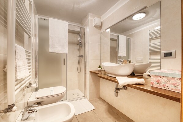 Un baño moderno con ducha de vidrio, lavamanos blanco y bidé.