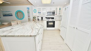 A modern kitchen with white cabinetry, a marble countertop, a built-in oven, and a microwave. - 🌊Updated Oceanfront Condo-Chadham by the Sea 119🌊 (New Smyrna Beach)