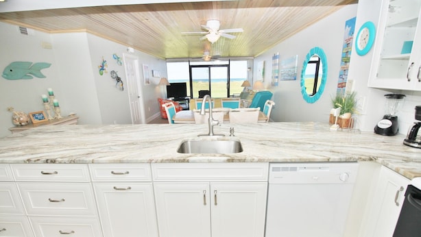 A kitchen with white cabinets, a marble countertop, and a dishwasher. - 🌊Updated Oceanfront Condo-Chadham by the Sea 119🌊 (New Smyrna Beach)