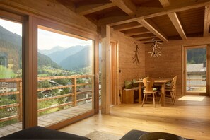A wooden interior with a dining area, large windows offering a mountain view, and a hanging decoration. - 1112 Hinterstoba (Gaschurn)