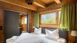 Un dormitorio de cabaña de madera con una cama grande, cortinas verdes y una ventana con vistas a la vegetación.
