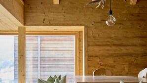 Et træinteriør med højt til loftet, et spisebord, bænke og en hængende lampe.