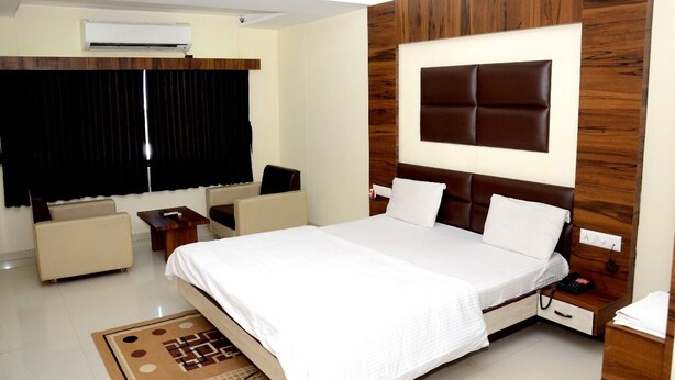 A modern hotel room with a large bed, a wooden accent wall, a flat-screen TV, and a small seating area. - The New Holiday II (Mahesana)