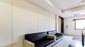 A modern waiting area with a sofa and a bench, a glass door leading to a staircase, and a view of the outside. - The New Holiday II (Mahesana)