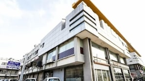 A modern multi-story building with large windows and a prominent yellow structural element. - The New Holiday II (Mahesana)