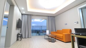 A modern hotel room with a balcony, a sofa, a coffee table, a TV, and a laptop on a desk. - Dasan Beache Golf & Resort (Gangjin)