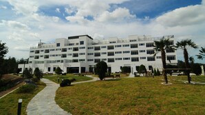 A multi-story building with a modern architectural design, featuring a central courtyard with pathways, benches, and palm trees. - Dasan Beache Golf & Resort (Gangjin)