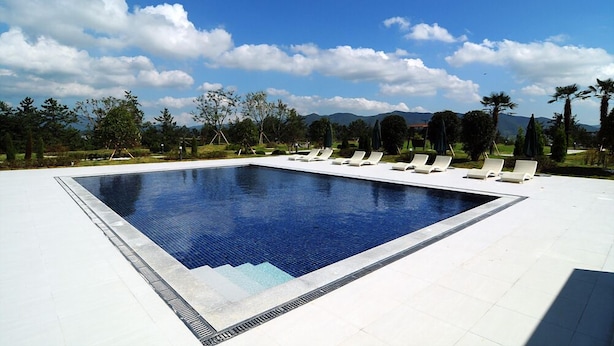 A rectangular swimming pool with a tiled edge, surrounded by white lounge chairs and a clear blue sky with clouds. - Dasan Beache Golf & Resort (Gangjin)