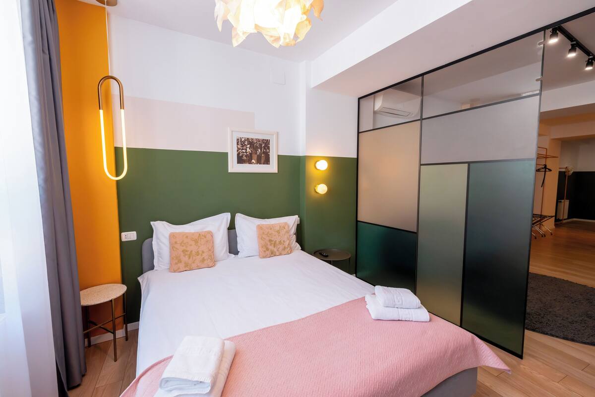 A modern hotel room with a bed, a chair, a desk, and a mirror.