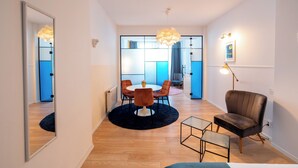 Ein modernes Wohnzimmer mit rundem Tisch, zwei Stühlen, einer Couch, einer Stehlampe und einem Spiegel.