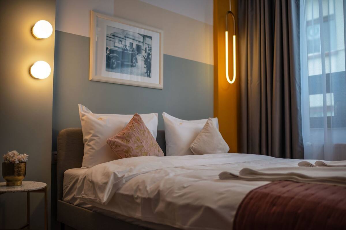 A neatly made bed with white linens, a framed photograph on the wall, and a bedside table with a vase of flowers.