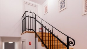Eine Treppe mit schwarzen Geländern und Holzstufen, ein Feuerlöscher und gerahmte Kunstwerke an den Wänden.