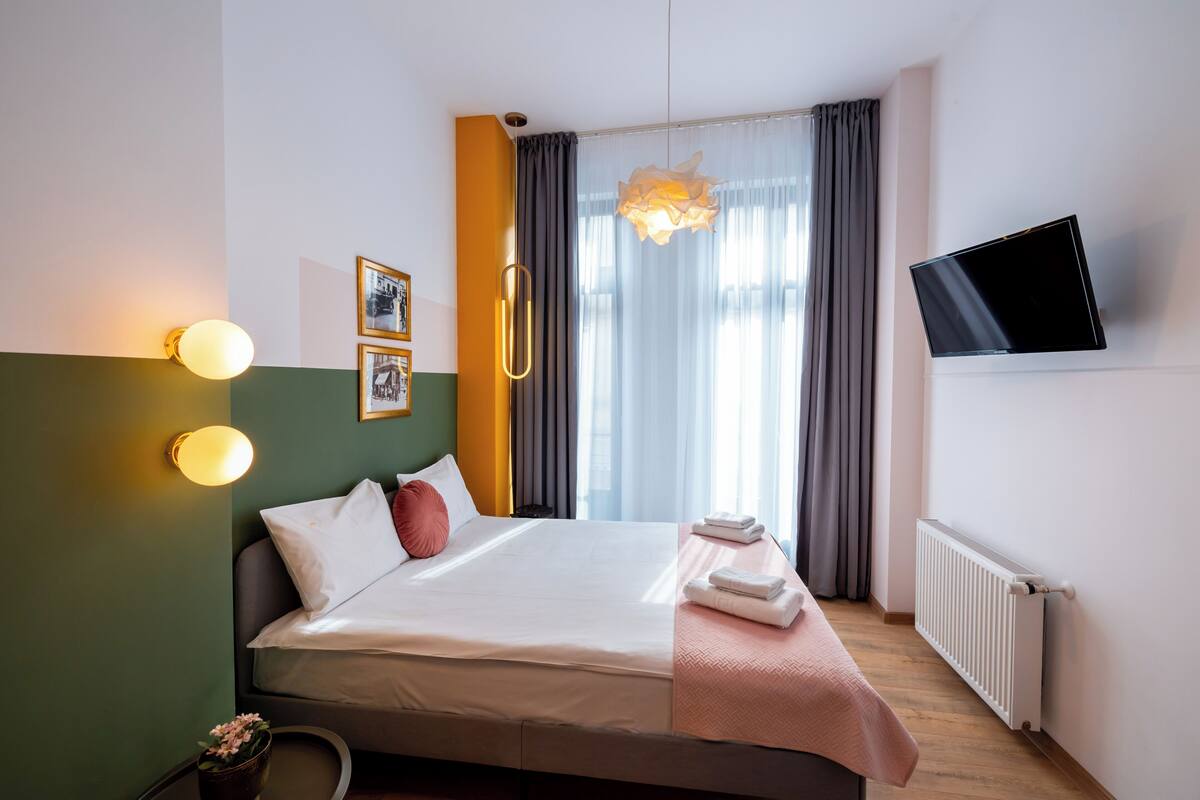 A hotel room with a bed, bedside lamps, a flat-screen TV, and a window with curtains.