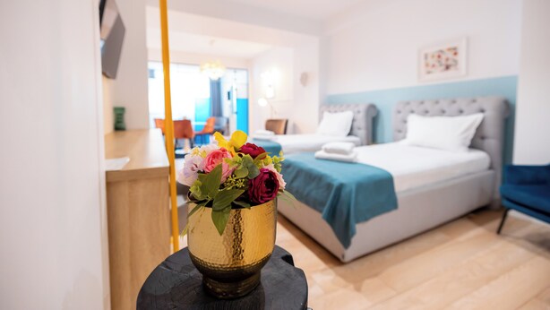 Ein Hotelzimmer mit Bett, Nachttisch mit Blumenvase und Blick ins Zimmerinnere.