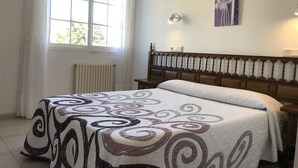 Un dormitorio con una cama grande, una ventana con cortinas, un radiador y una lámpara fijada a la pared.