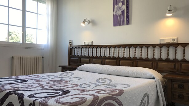 Un dormitorio con una cama, un radiador, una ventana y una lámpara fijada a la pared.
