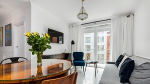 Ett modernt vardagsrum med ett matbord i glas, en blå fåtölj och en grå soffa med en dekorativ prydnadskudde.