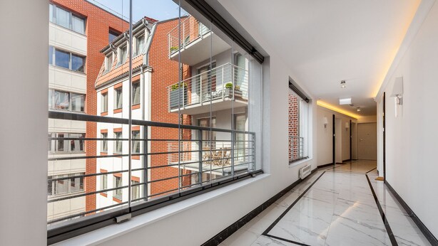 En korridor med ett stort fönster som vetter mot en byggnad med rött tegel, ett marmorgolv och en modern inredning.