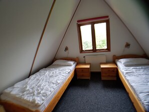 A small, triangular attic bedroom with two single beds, a window, and a radiator.