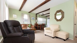 A living room with a black recliner, beige armchair, and a dining area with a table and chairs.