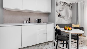 A modern kitchen with white cabinets, a black kettle, and a fruit bowl on a round table. - Happy Stay Old Town Tartaczna 26 A (Gdansk)