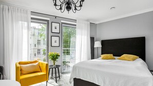 A modern hotel room with a large bed, a yellow armchair, a small round table, and a view of the city through large windows. - Happy Stay Old Town Tartaczna 26 A (Gdansk)