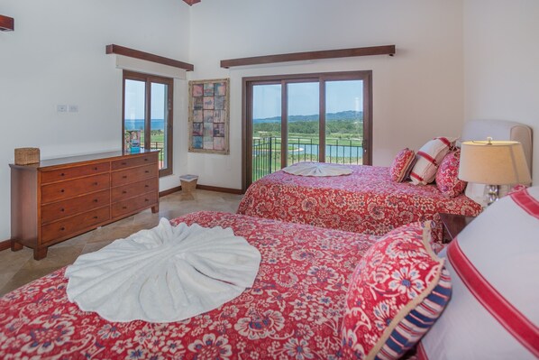 A bedroom with two beds, a dresser, and a view of a landscape. - Pristine Bay 4033 4 Bedroom Home by RedAwning (Roatan)