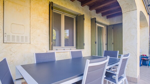 An outdoor patio with a table and chairs, a window with shutters, and a door with a green shutter.
