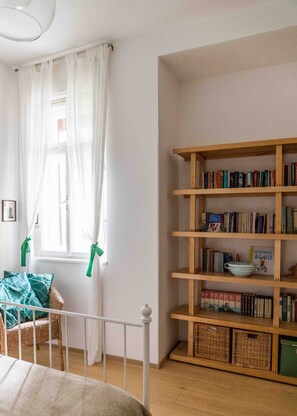 Quarto com berço branco, estante de madeira e janela com cortinas brancas amarradas com fitas verdes.