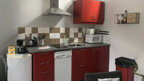 Une cuisine de taille réduite avec des meubles de rangement rouges, un four à micro-ondes, une machine à café et un lave-vaisselle.