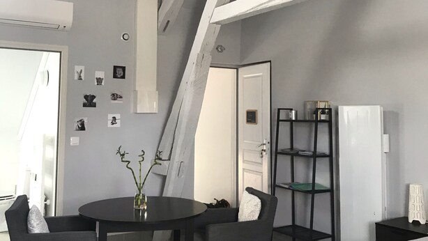 Une chambre moderne avec un plafond en pente, un lit avec un matelas blanc, une tête de lit en bois, une table de chevet et une commode.