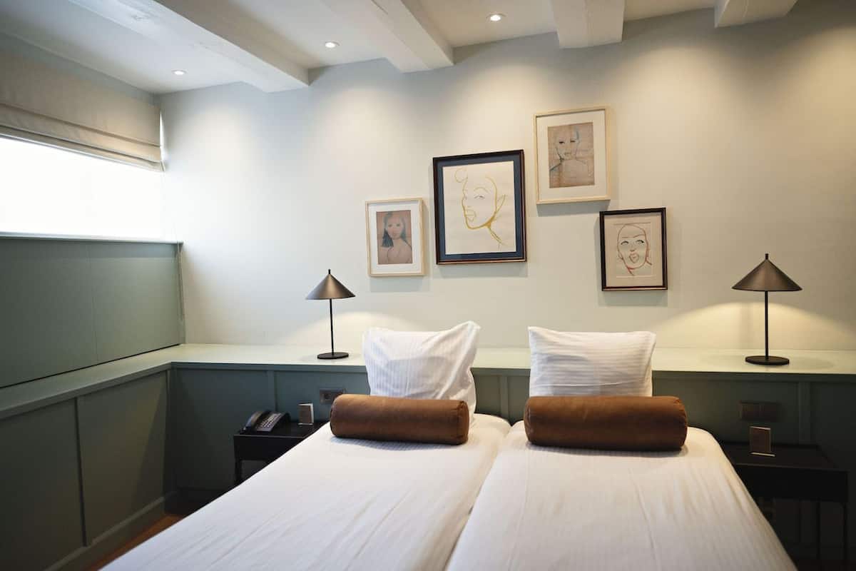 A hotel room with two beds, a desk, and artwork on the wall.