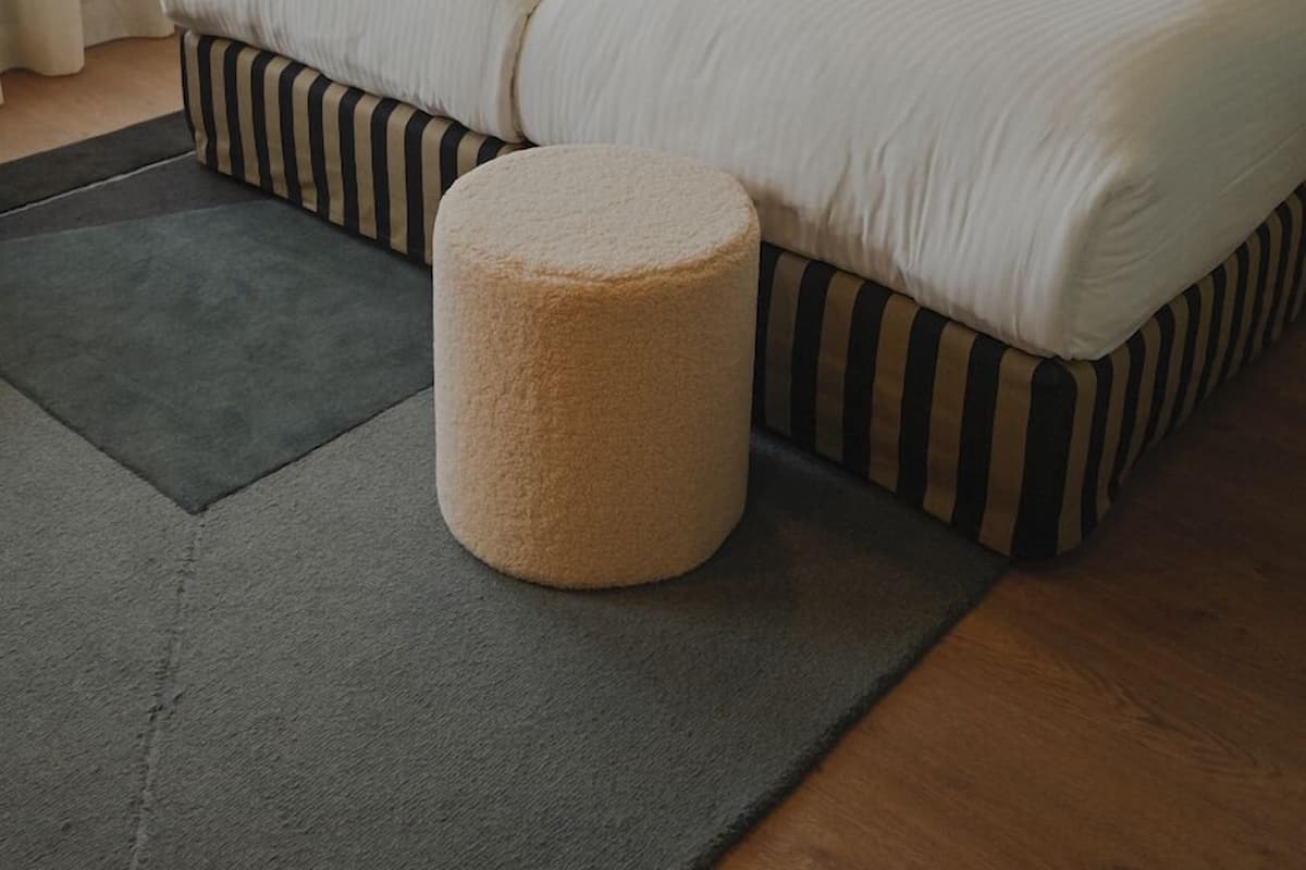 A hotel room with two beds, a bedside table, a lamp, a rug, and a painting on the wall.