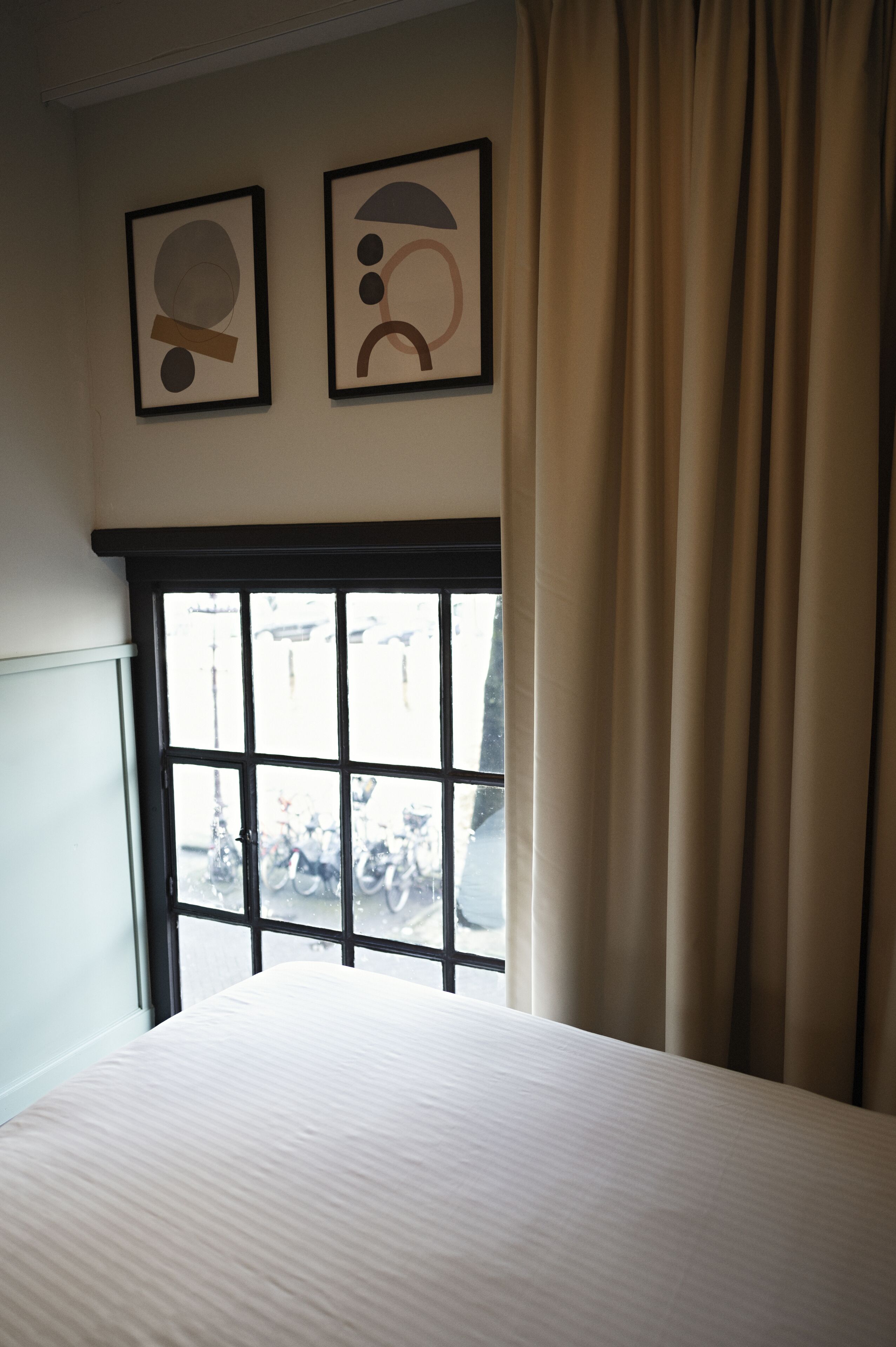 Una habitación de hotel con una cama, un ventanal con cortinas y dos obras de arte abstracto enmarcadas en la pared.