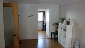 A hallway with wooden flooring, a white door, a white shelving unit with plants, and a radiator. -  Keybutler City Apartment Henrik Wergelands (Kristiansand)