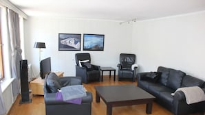 A living room with a sofa, two armchairs, a coffee table, and a TV stand. There are two framed pictures on the wall. -  Keybutler City Apartment Henrik Wergelands (Kristiansand)