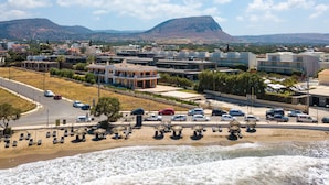 Un pueblo costero con una playa, coches aparcados a lo largo de la orilla y edificios al fondo.