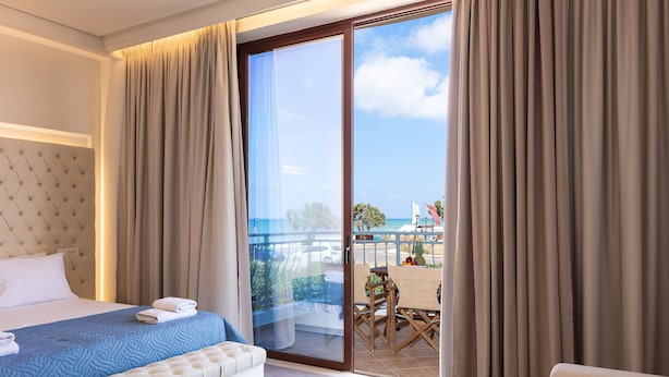 Una habitación de hotel con cama, sofá, balcón con mesa y sillas, y cortinas.