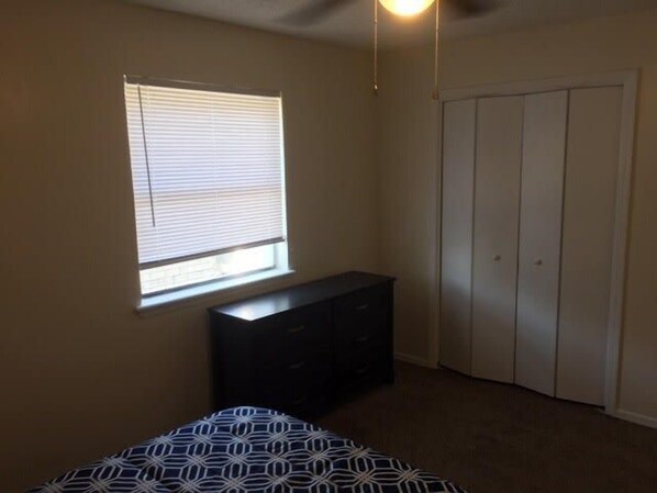 A bedroom with a bed, a dresser, a closet, and a window with blinds.