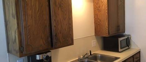 A kitchen with wooden cabinets, a microwave, a coffee maker, and a double sink.