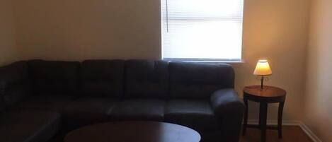 A living room with a dark-colored sofa, a round coffee table, and a lamp on a small table.