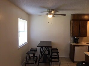 Una cocina compacta con una mesa de comedor y taburetes, un ventilador de techo y armarios de madera.